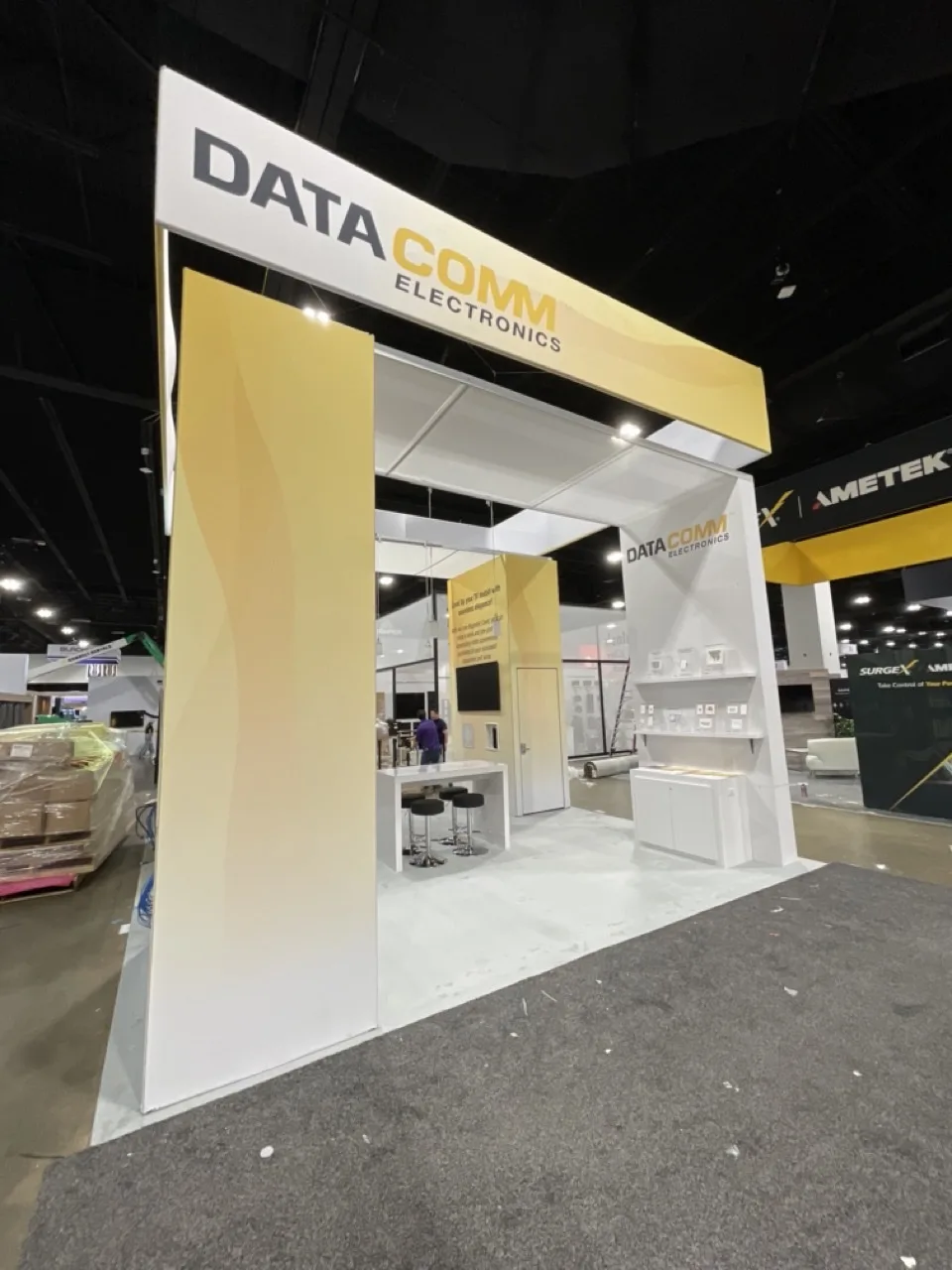 White-framed exhibit with yellow overhead signage and product displays